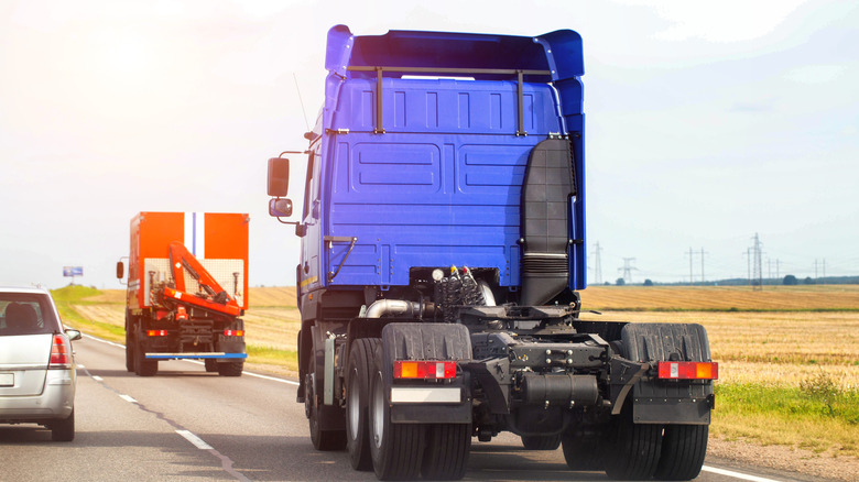 Blue semi-truck driving in mixed traffic on highway, rear view