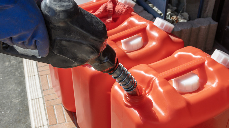 Person filling gasoline in plastic containers at a fuel pump in Japan.