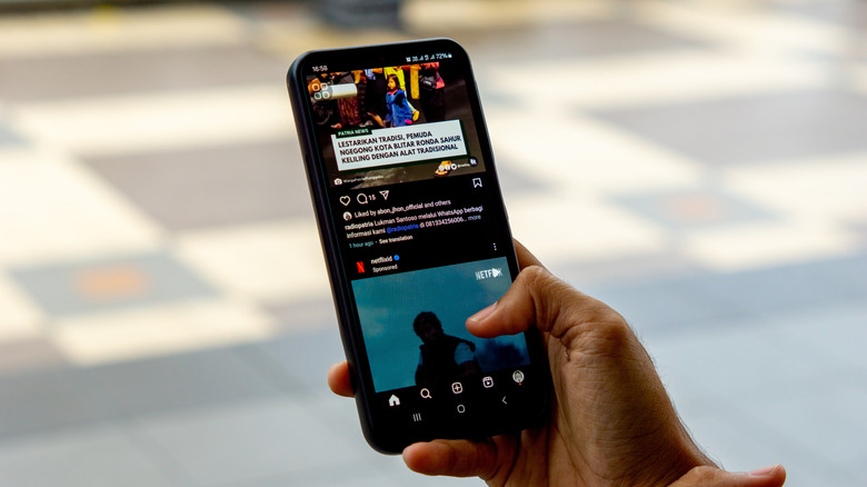 A hand scrolling an Instagram feed on an Android smartphone.