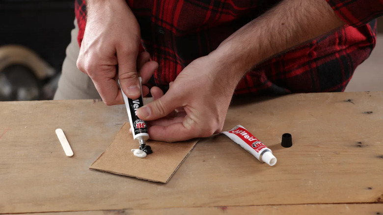 A man using J-B Weld on cardboard at a work table