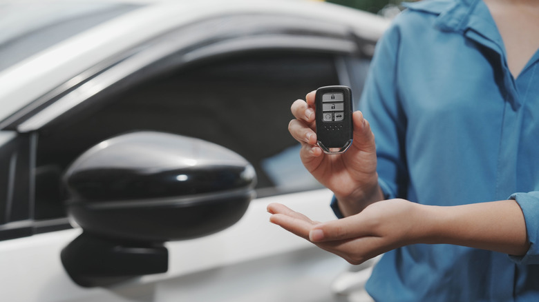 A woman showing off a car key fob next to her vehicle.