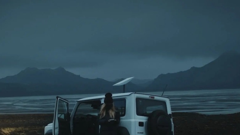 Woman standing outside a vehicle with Starlink on the roof and cloudy skies in the background