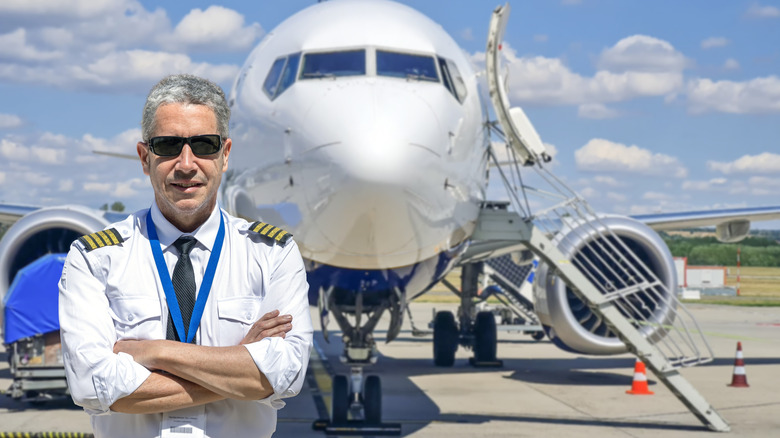 A commercial airline pilot stands confidently in front of a passenger jet.