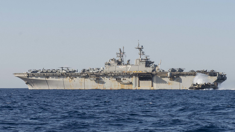 An amphibious assault ship at sea with a hover craft departing