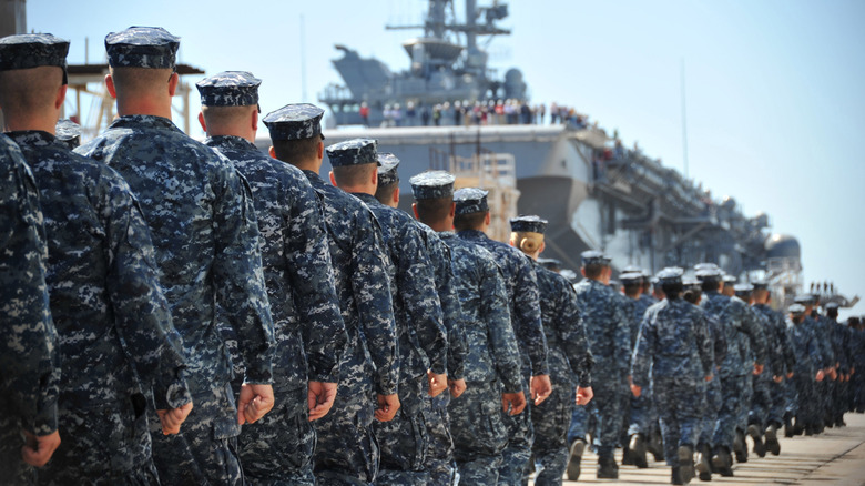 Marines lined up in formation, boarding an amphibious assault ship