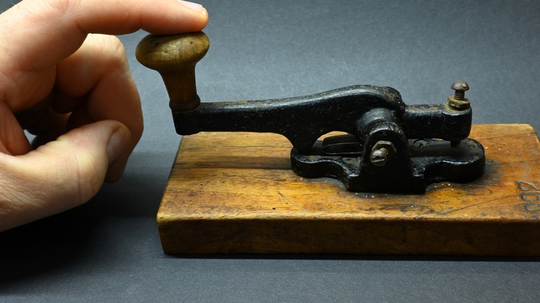 A finger tapping an old telegraph key on wood block