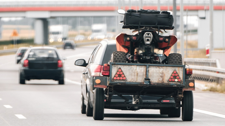 An ATV trailer connected to a minivan driving down the highway