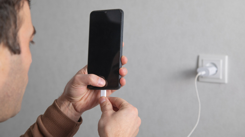 Person charging a smartphone plugged into a wall outlet.