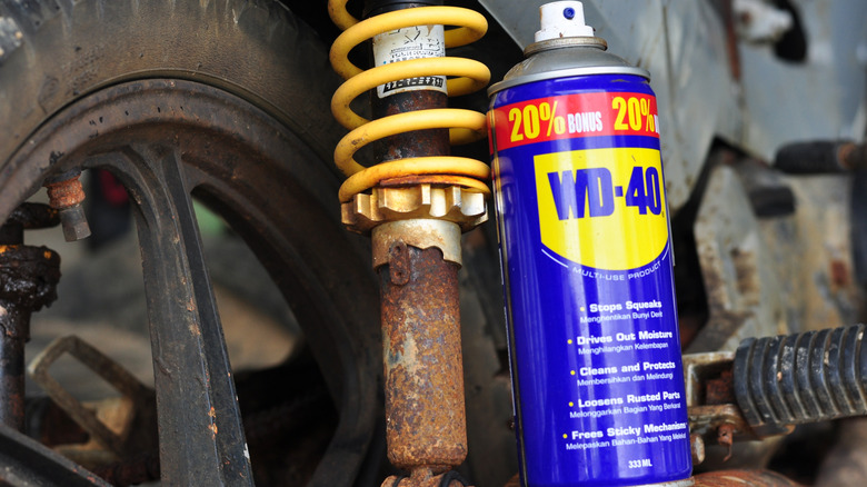 A can of WD-40 next to a rusty vehicle.