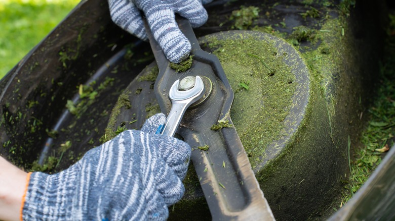 A person removing a lawn mower blade.