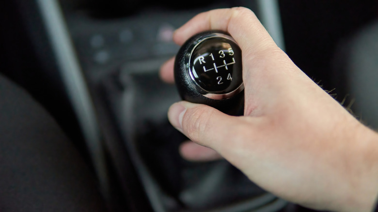 A person holding a five-speed manual shifter, close focus