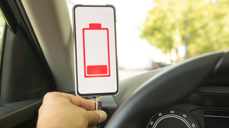 a person in a car plugging in a USB-C cord to a smartphone with a low battery indication