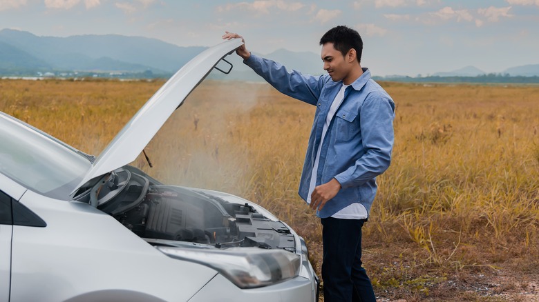 Man inspecting a broken down car with engine overheating