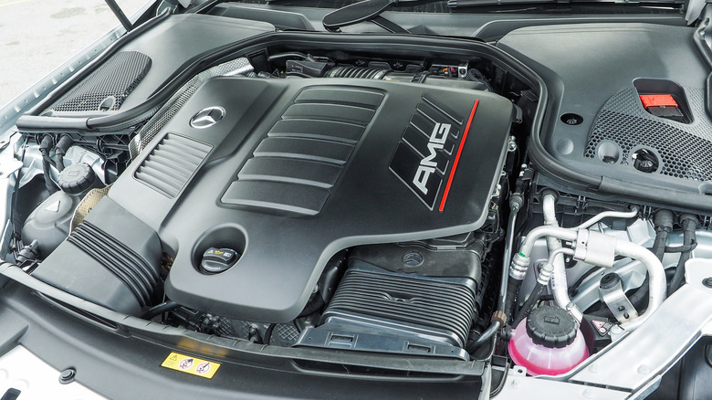 View under a car hood shows a black plastic engine cover bearing AMG insignia.