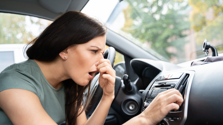 A lady holding her nose while adjusting car's air-conditioning vent