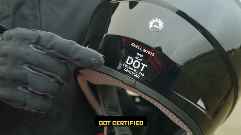 Gloved finger pointing to a DOT certification label on the back of a motorcycle helmet.
