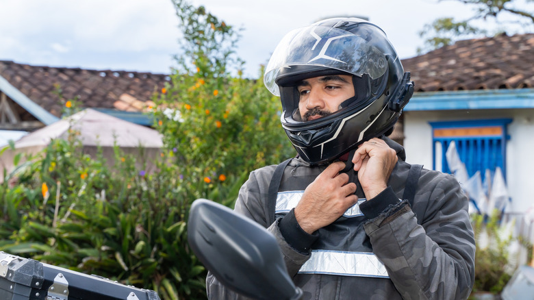 A rider securing his helmet strap before hopping onto his motorcycle.