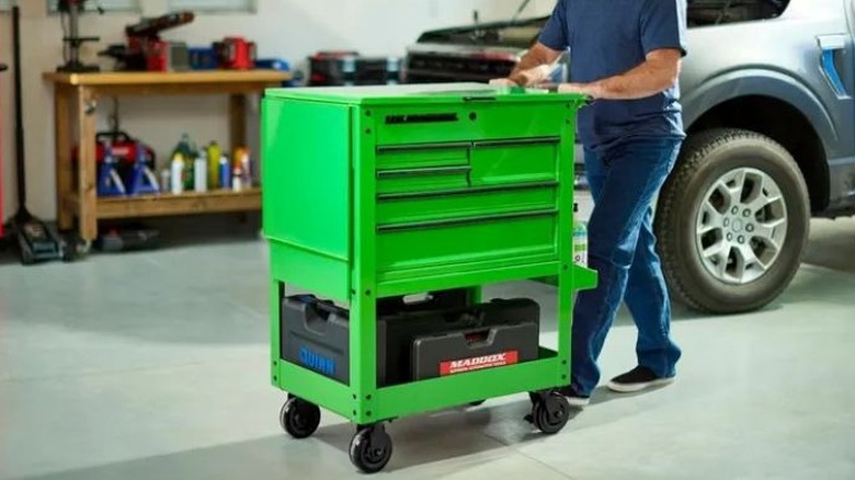 A person pushing a green tool cart in a garage