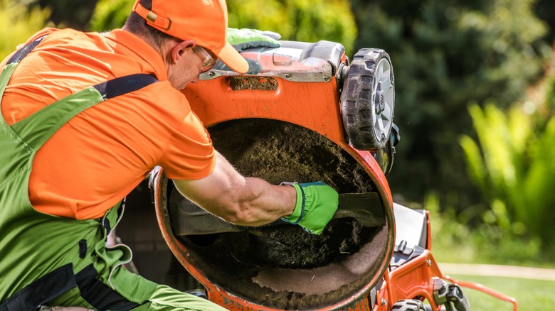 A man cleaning the underside of a push lawn mower.
