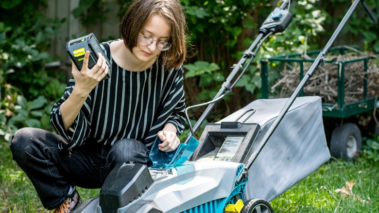 A woman with glasses removing the battery from an electric push mower.