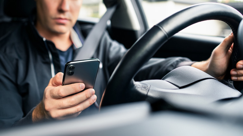 A driver holding a smartphone in their right hand.
