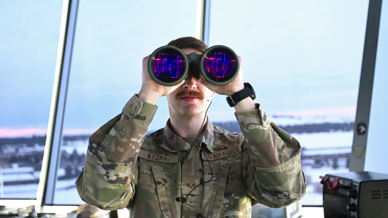 A U.S. Air Force air traffic controller looking through large binoculars from airport control tower