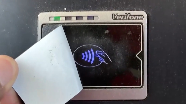 Person peeling off tap-to-pay sticker on gas pump