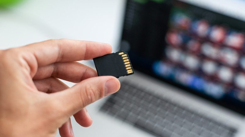 A person holding SD card with laptop in the background