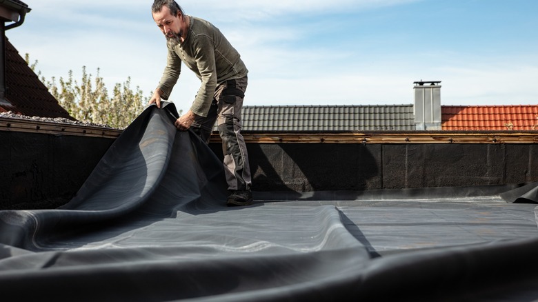 Man adjusting black tarp on roof