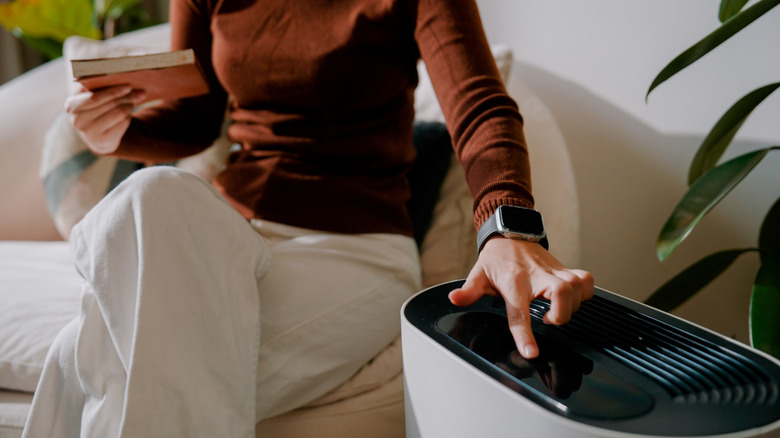Close-up of person turning on portable air conditioner while sitting on couch and reading book.