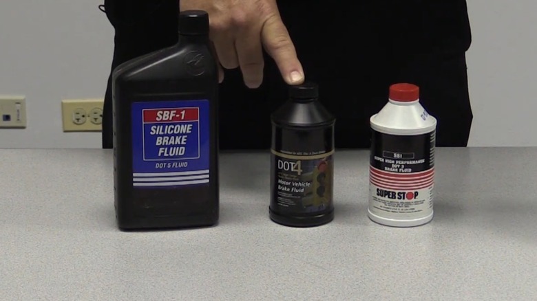 An image showing a person pointing at bottles of dot 5, dot 4, and dot 3 brake fluid