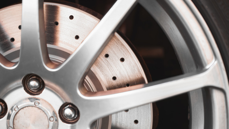 Close-up of drilled brake rotor behind car rim