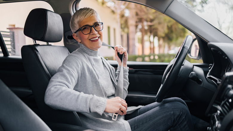 Portrait of happy senior woman fastening seat belt before driving a car.