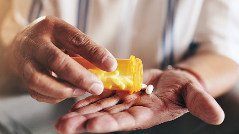 Closeup of a person's hands taking out pills from a bottle.