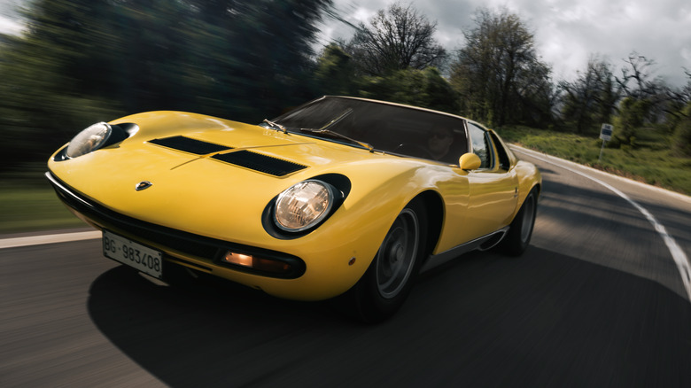 A yellow Lamborghini Miura driving in the sun.