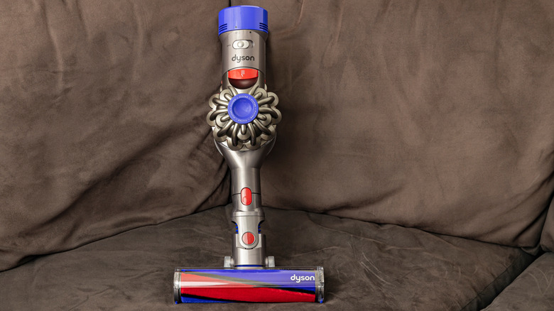 A compact Dyson V8 vacuum cleaner on a brown couch