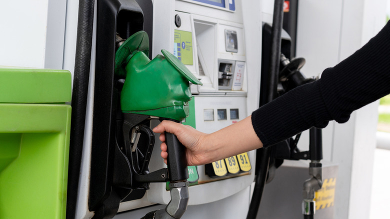 Close up of a woman lifting a gasoline nozzle from a fuel pump