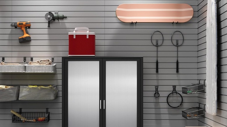 Badminton rackets, drills, and a skateboard hang on a slat wall