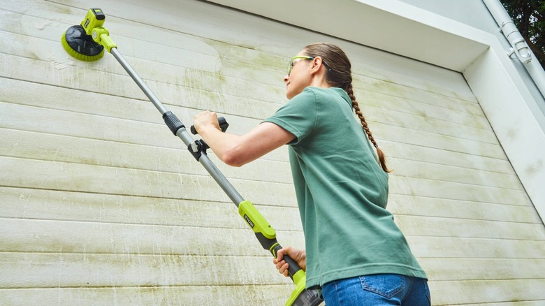 A woman uses a telescoping power scrubber on the side of a bulding