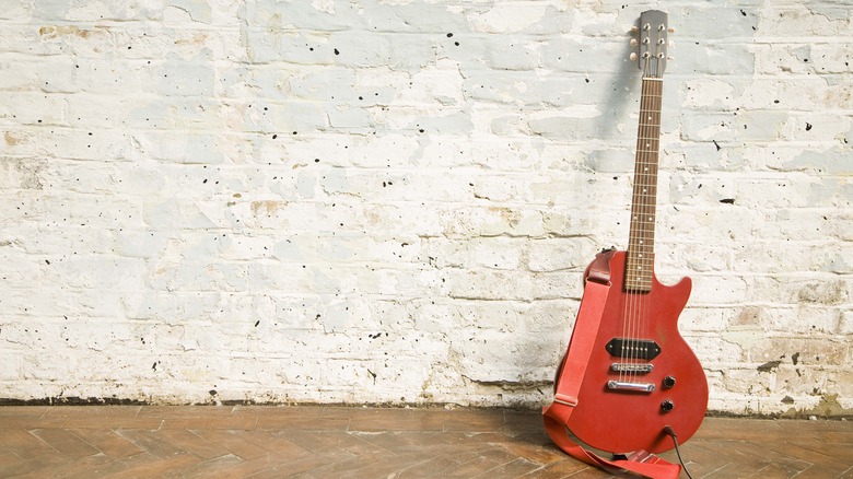 Solid-body orange electric guitar against white wall 