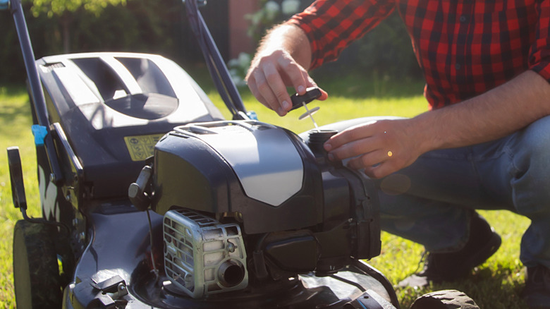 Man checking gas lawn mower engine in the yard