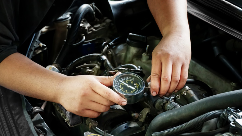 Mechanic servicing car using analogue compression tester