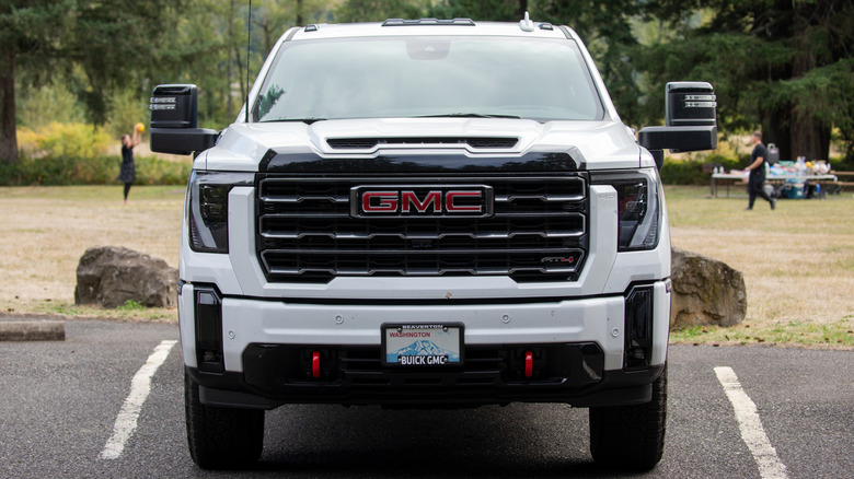 A white diesel GMC Sierra heavy-duty truck parked head-on with trees and grass in the background, front view