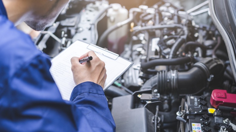 Mechanic checking an engine while scribbling on note pad