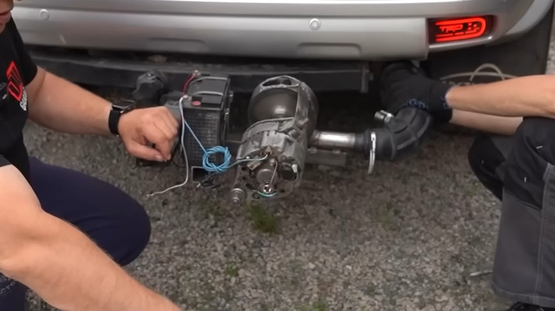 An exhaust-powered alternator at the back of a Toyota SUV with a mechanic kneeling next to it