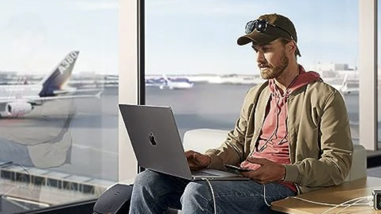 A man charging a MacBook at an airport with an Anker Prime Power Bank.