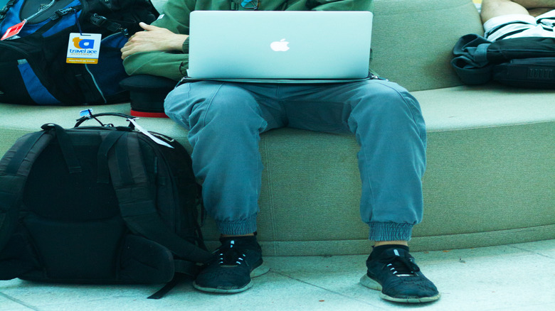A man using a MacBook on his lap in an airport.
