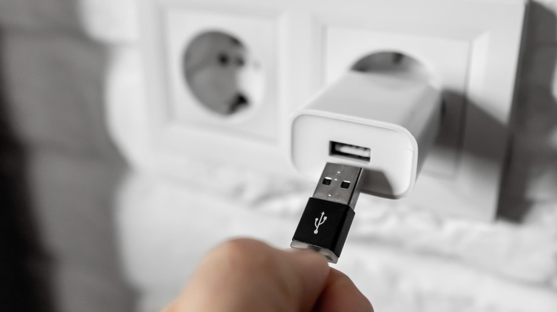 Man inserting a USB cable into a wall charger.