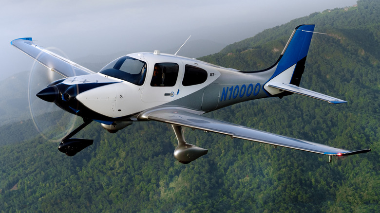 A Cirrus SR22 flies across a wooded landscape