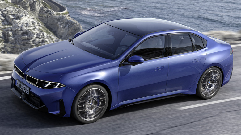A BMW i3 sedan in Le Castellet Blue, being driven next to water and rocks